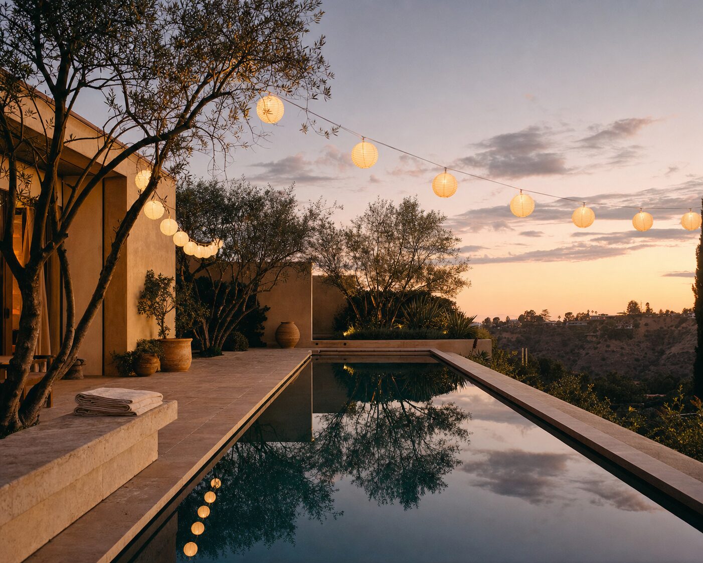 Lap pool at dusk with paper lanterns strung between olive trees